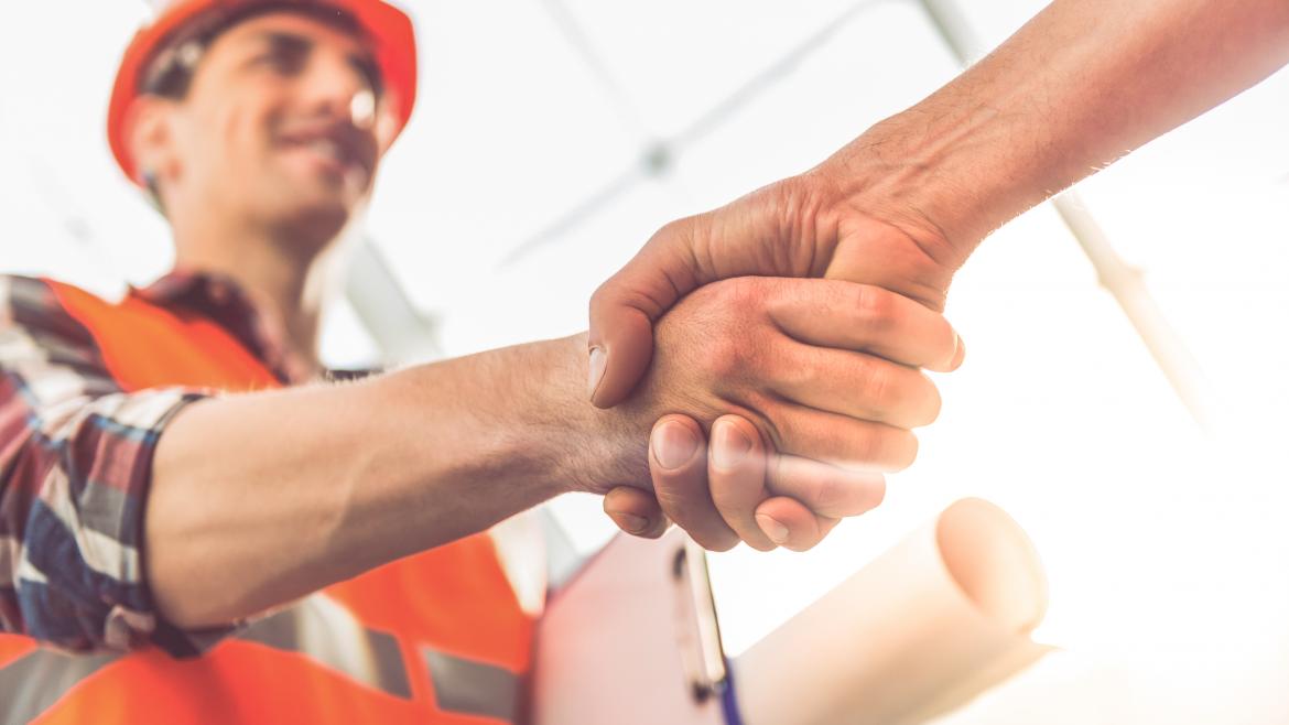 Saludo laboral Un hombre con un casco de obra da la mano a otro hombre