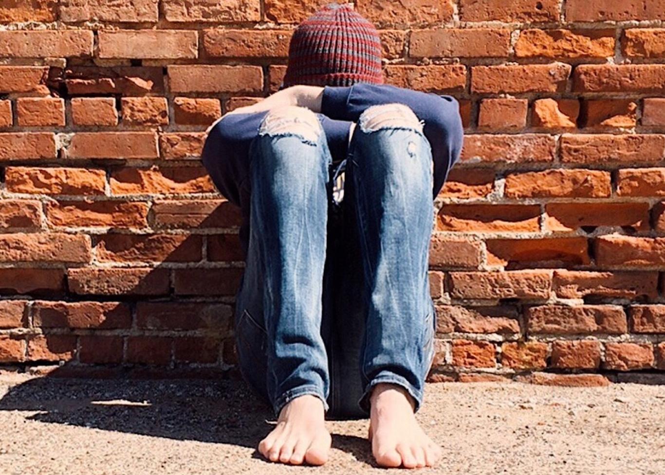 Acoso escolar Chico sentado en el suelo apoyado en la pared y tapándose la cara