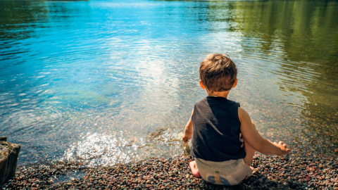 niño agachado en la orilla de un lago