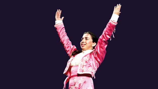 Bailaora de flamenco con los brazos en alto sobre fondo negro