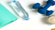 Imagen de una esterilla, una botella de agua, unas pesas azules y un plátano.