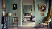 Interior de una casa antigua con mobiliario envejecido y paredes en color verde llenas de lienzos enmarcados con cuadros del siglo XIX