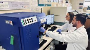 Un hombre y en segundo plano una mujer trabajando en una máquina en un laboratorio