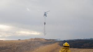 Un bombero de la Comunidad de Madrid y un helicoptero volando en el cielo mientras suelta agua