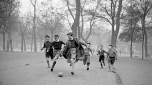 Fotografía antigua en blanco y negro de unos niños en un bosque jugando al fútbol