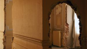 Una pared con una rotura a través de la que se observa una sala con parede corroídas