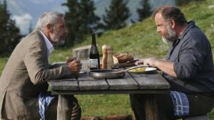 Fotograma del largometraje muestra a dos hombre comiendo en un prado sobre una mesa de madera