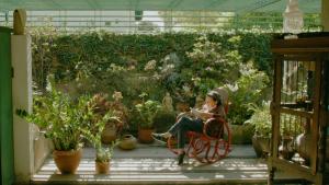 imagen de una mujer en una mecedora leyendo en jardín lleno de flores y plantas