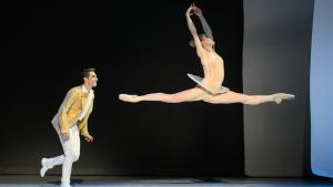 Bailarina de ballet realizando un gran salto en el aire mientras un bailarín la observa en un escenario de teatro
