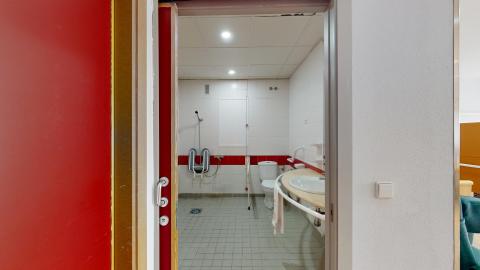 Baño y aseo accesibles dentro de la habitación. La puerta de acceso es corrediza. A la derecha está el lavabo con espejo y al fondo a la derecha el inodoro. Al fondo a la izquierda está la ducha con plena accesibilidad.