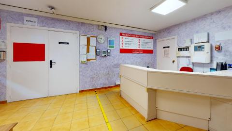 Vista de la esquina del mostrador de recepción en blanco. A la izquierda el acceso a fisioterapia a través de puertas blancas. En ese mismo muro hacia la derecha, detrás del mostrador, el directorio. A la derecha la zona detrás del mostrador y una puerta de acceso restringido. 