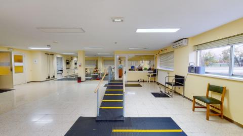 Fisioterapia. Amplia sala de fisioterapia con estaciones para ejercicios de brazos, de piernas, de rampa, escalones y masajes, entre otros. En color amarillo claro y ventanas en dos de los cuatro muros. Muy luminoso y ventilado.