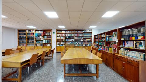 Biblioteca. Amplio espacio con dos muros con libreros de madera. Al centro, tres grandes mesas rectangulares de madera con sillas.