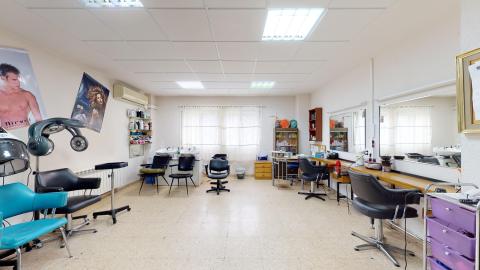 Peluquería. Espacio blanco y luminoso. Al fondo una gran ventana con cortina blanca. Enfrente, tres estaciones de lavado. A la derecha espejos y dos estaciones de corte. A la izquierda dos estaciones de secado.