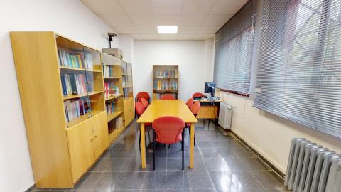 Biblioteca. Sala alargada pintada en blanco. A la derecha ventanas a todo lo largo del muro. A la izquierda y al fondo, libreros de madera. En la esquina del fondo a la derecha, un escritorio con ordenador y al centro una mesa de madera con ocho sillas.