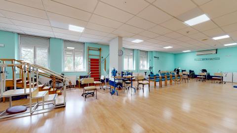 Fisioterapia. Amplia sala luminosa con tarima y muros en verde azulado. Se distribuyen diversas estaciones para la realización de ejercicios específicos.