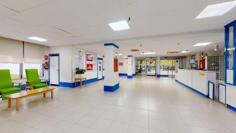 Acceso y recepción. Vista complementaria de la sala de estar que une los sillones verdes con el ventanal de control, que es parte de la recepción, con las puertas de cristal de acceso desde el exterior.