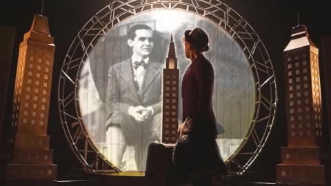 imagen de escena, muestra un hombre en mitad de un escenario que recrea la ciudad de Nueva York y de fondo una fotografía de Lorca proyectada