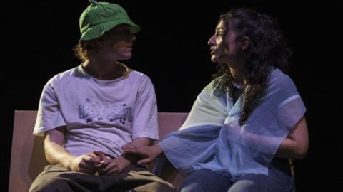 Imagen de escena muestra un pareja adolescente de un chico y una chica sentados charlando en un banco
