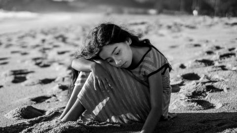 Imagen de chica sentada en la playa con aspecto pensativo