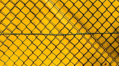 Detalle de una verja cruzada con un fondo amarillo