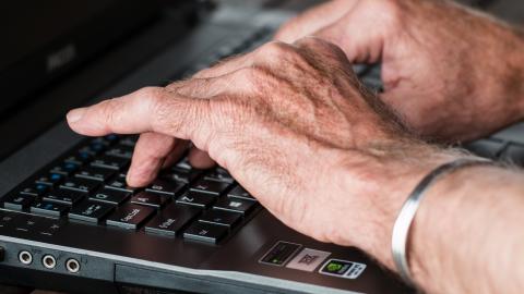 Primer plano de las manos de un hombre mayor sobre teclado de ordenador portátil