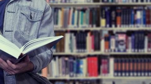 Documentación Persona en una biblioteca sosteniendo un libro