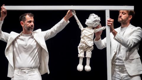 imagen de dos hombres vestidos de color blanco sujetando un títere de un niño todo color blanco