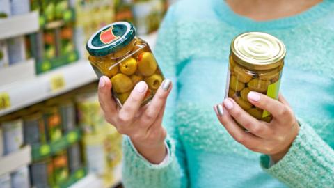 Etiquetado de alimentos Mujer comparando el etiquetado de dos botes de aceitunas en un supermercado