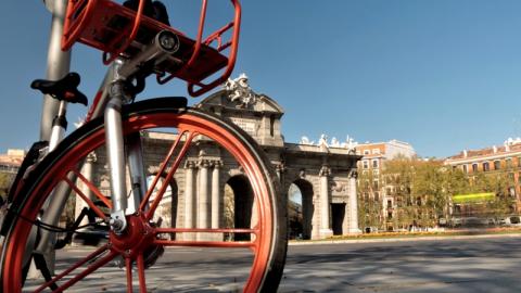 IMAGEN DE LA PUESTA DE ALCALÁ VISTA TRAS LOS RADIO DE LA RUEDA DE UNA BICICLETA ROJA