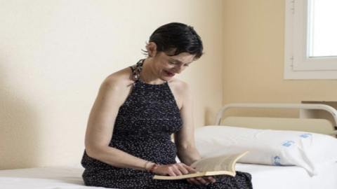 Mujer sentada leyendo un libro sobre la cama de un hospital
