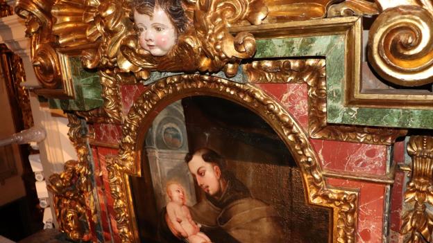 imagen de un fragmento de retablo con una cabeza de ángel esculpida y una pintura insertada en marco decorado