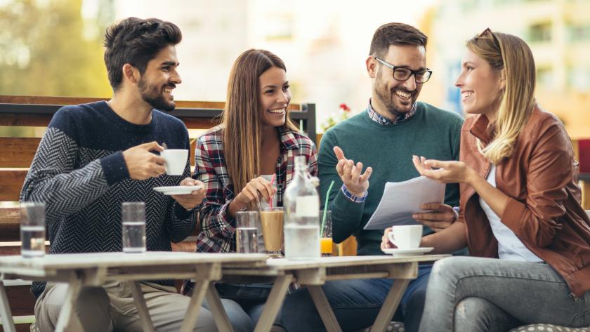 cuatro chicas y chicos jóvenes sentados tomando café sonrientes