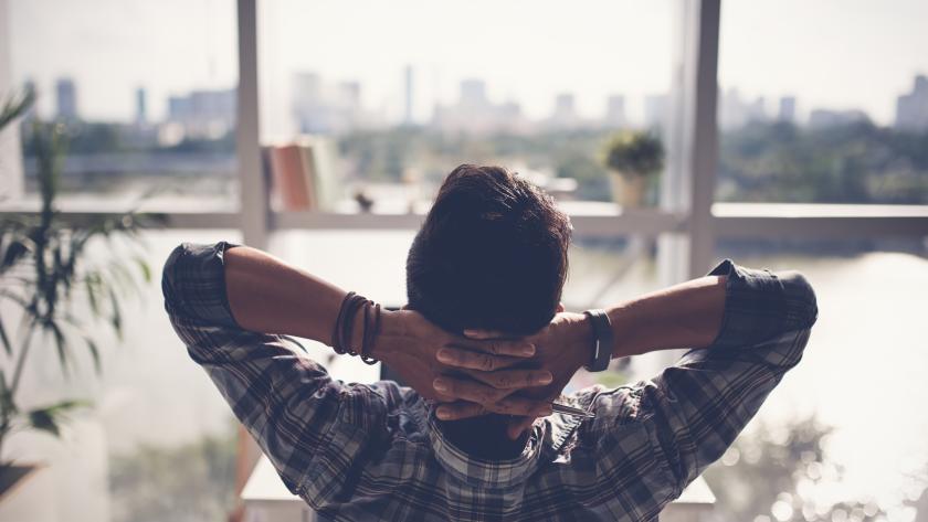 hombre relajado sentado mirando hacia la ventana con las manos entrelazadas detrás de la cabeza