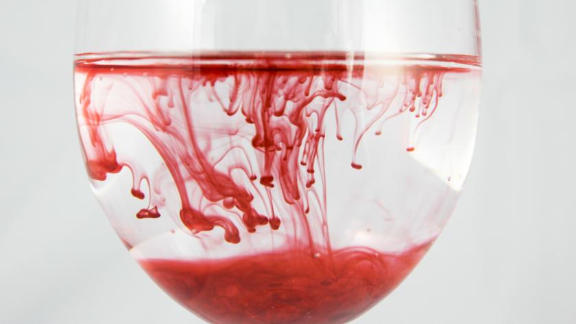 Copa de agua con un líquido rojo disuelto formando ondas
