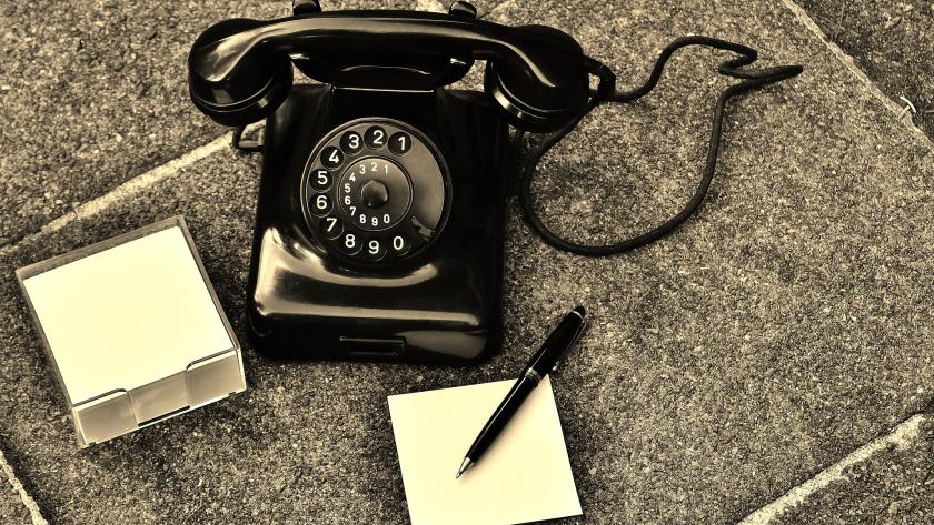 Teléfono antiguo negro de mesa junto a tacos de notas y un bolígrafo