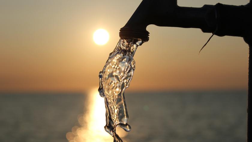 agua saliendo de un grifo con el atardecer de fondo
