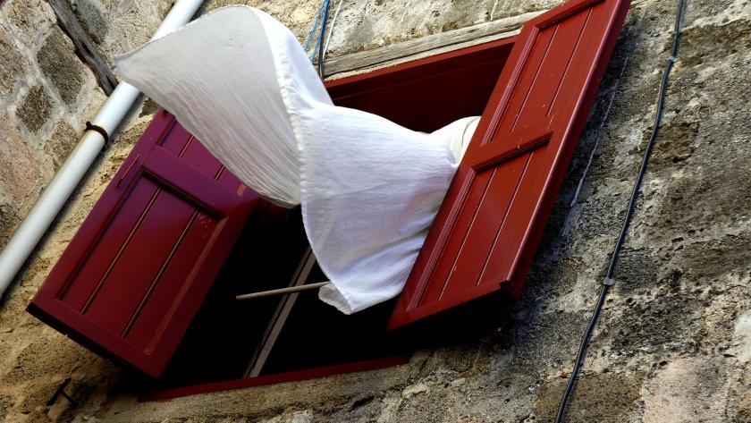 Fachada de una casa antigua con las ventanas abiertas y la cortina moviéndose por el viento