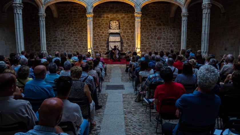 Un patio de un castillo con gente sentada en sillas y al fondo el músico tocando un instrumento