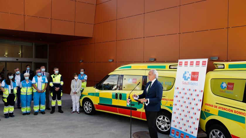 El consejero con un photocall de Salud Madrid y una ambulancia detrás interviniendo en el atril ante un grupo numero de componentes del 112