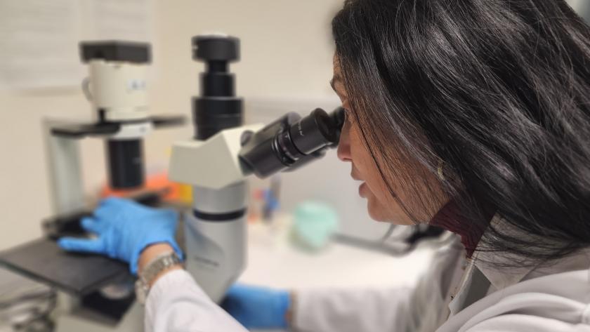 Mujer morena con bata blanca inclinada sobre microscopio