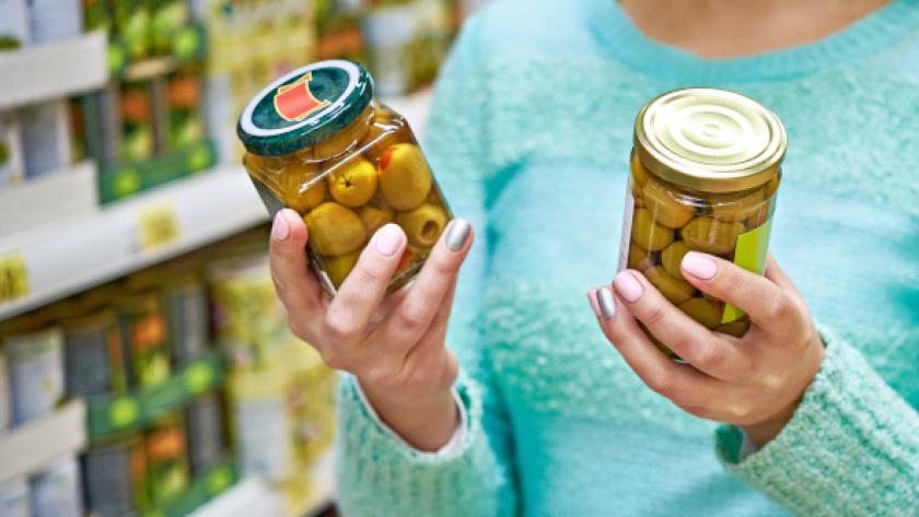 Mujer comparando el etiquetado de dos botes de aceitunas en un supermercado