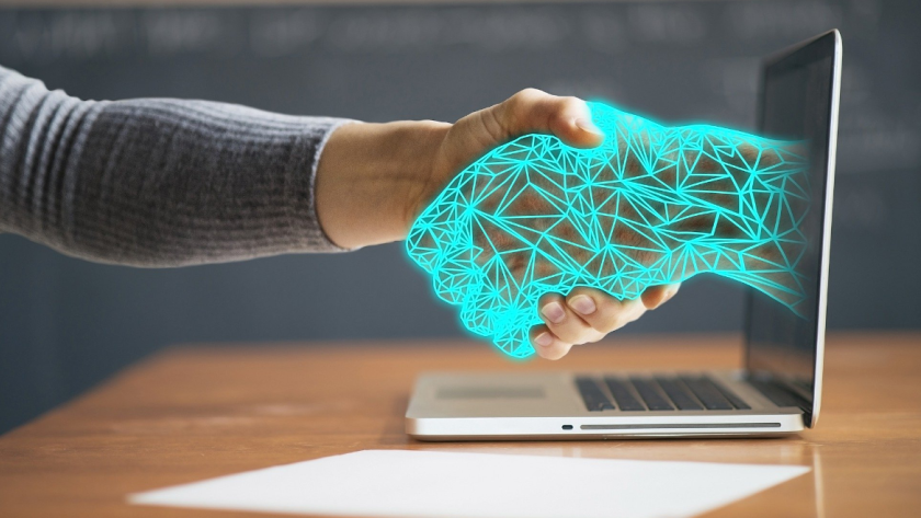 Imagen de una mano humana estrechando una mano virtual sobre una computadora