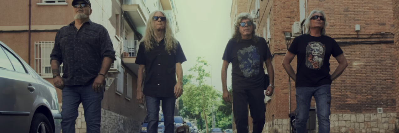 Fotograma del documental que muestra a los cuatro miembros de la agrupación musical paseando por un paisaje de barrio madrileño