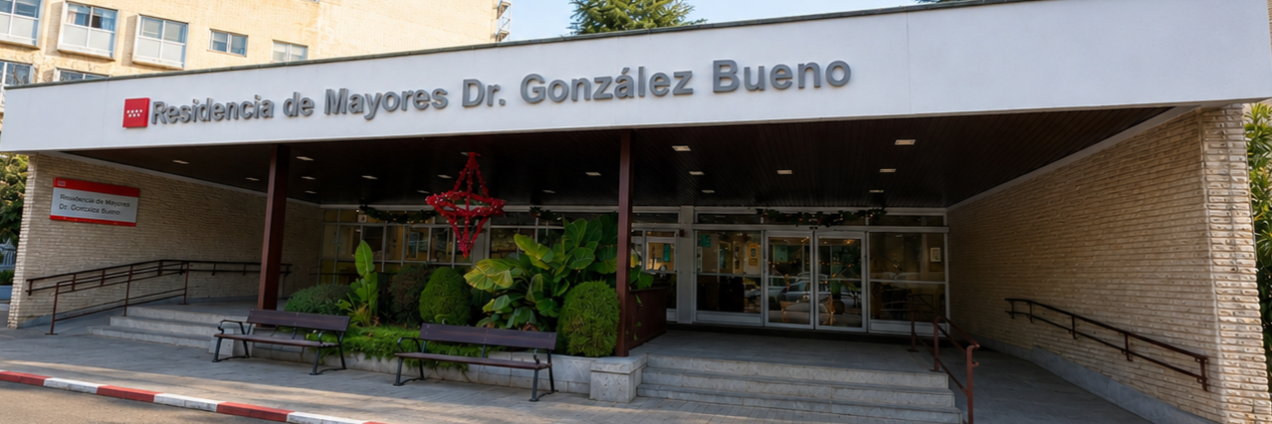 Fachada frontal de la residencia con una gran marquesina al centro con el nombre, puertas de cristal y jardinera central. A los lados edificios más altos. 