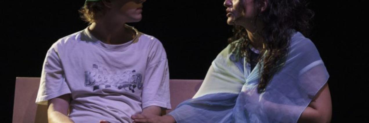 Imagen de escena muestra un pareja adolescente de un chico y una chica sentados charlando en un banco