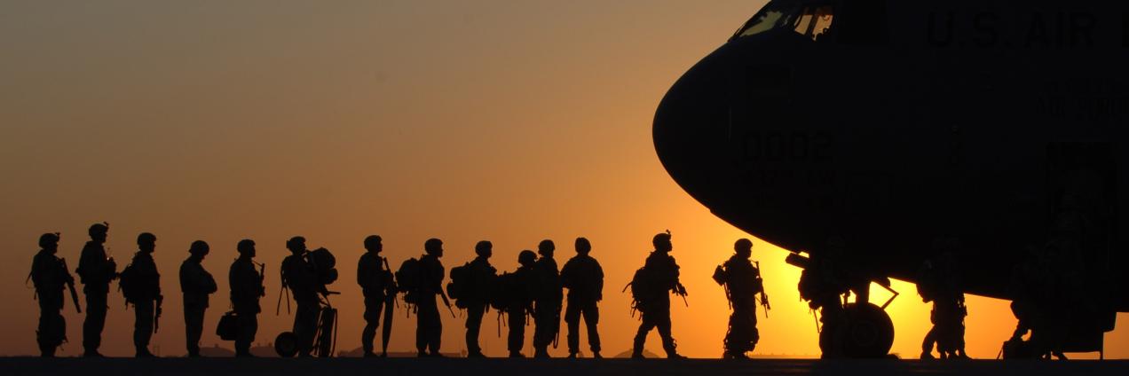 Militares con equipación de combate a contraluz junto a morro de avión