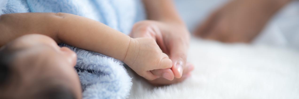 Plano de detalle de un adulto dando la mano a un bebe tumbado y tapado con una manta