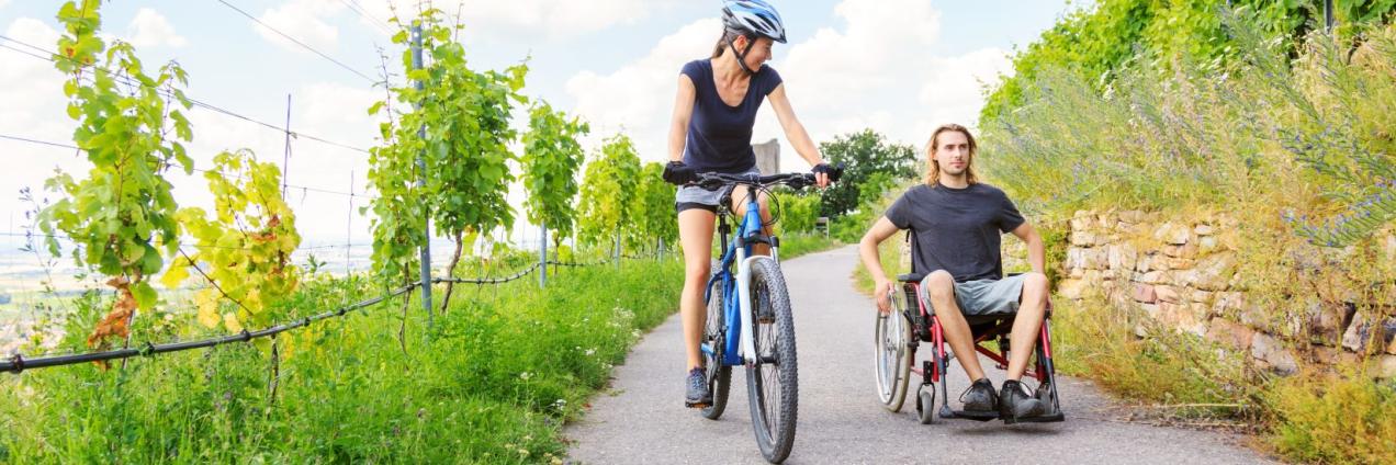 Mujer en bicicleta paseando junto a hombre en silla de ruedas