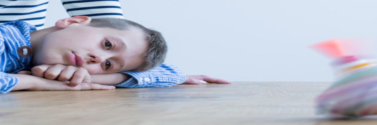Foto de niño autista acostado sobre una mesa con mirada perdida.
